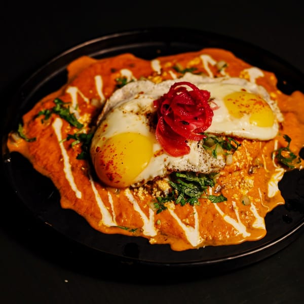 Que Vida Tacos' chilaquiles with two fried eggs, red sauce, crema, and pickled red onions.