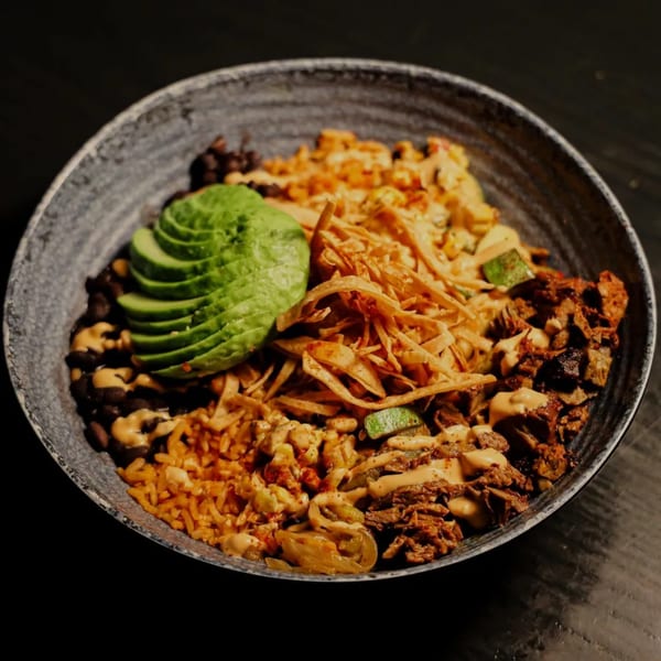 Que Vida Tacos' Mexican rice bowl with sliced avocado, black beans, and crispy tortilla strips.