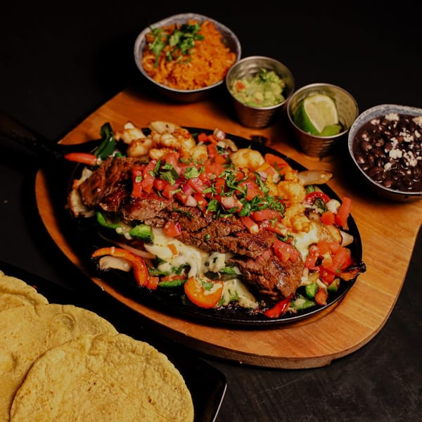 Sizzling Que Vida Tacos fajitas with steak, shrimp, vegetables, rice, beans, guacamole, and tortillas.