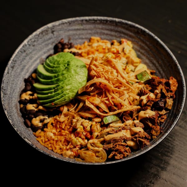 Que Vida Tacos' Mexican bowl with rice, beans, avocado, meat, and tortilla strips.