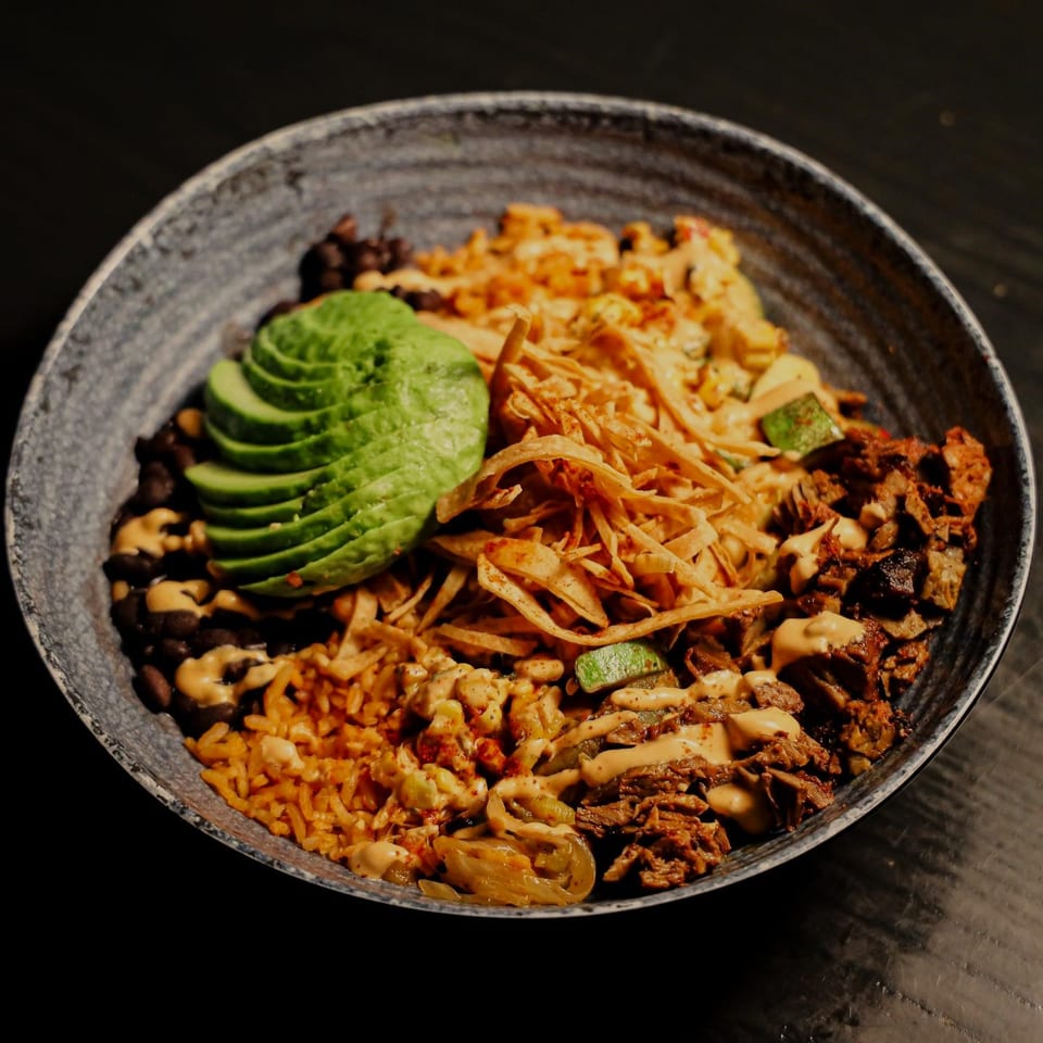 Que Vida Tacos' Mexican bowl with rice, beans, avocado, meat, and tortilla strips.